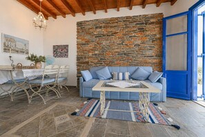 Une pièce avec un mur en pierre, une porte bleue, un canapé, une table et un lustre.