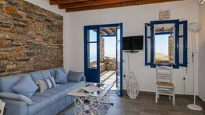 A room with a stone wall, a blue sofa, a table, a chair, and a TV. - Tzados Sunny Villa - Tinos Summer Retreat (Tinos)