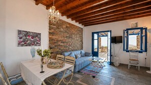 A rustic interior with exposed brick walls, a wooden ceiling, a dining area with a table and chairs, a blue sofa, and a television. - Tzados Sunny Villa - Tinos Summer Retreat (Tinos)