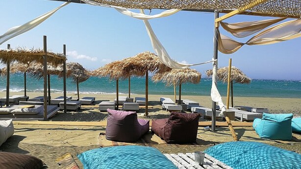 A beachside lounge area with thatched umbrellas, lounge chairs, and a pool. - Tzados Sunny Villa - Tinos Summer Retreat (Tinos)