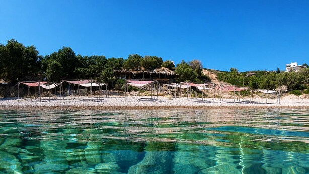 Una playa con agua cristalina, sombrillas y un edificio al fondo.