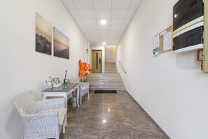Um corredor com escada, móveis de vime branco e obras de arte emolduradas nas paredes.