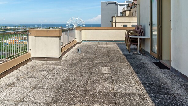 Un balcón con vista al mar y una noria, una silla y una mesa.