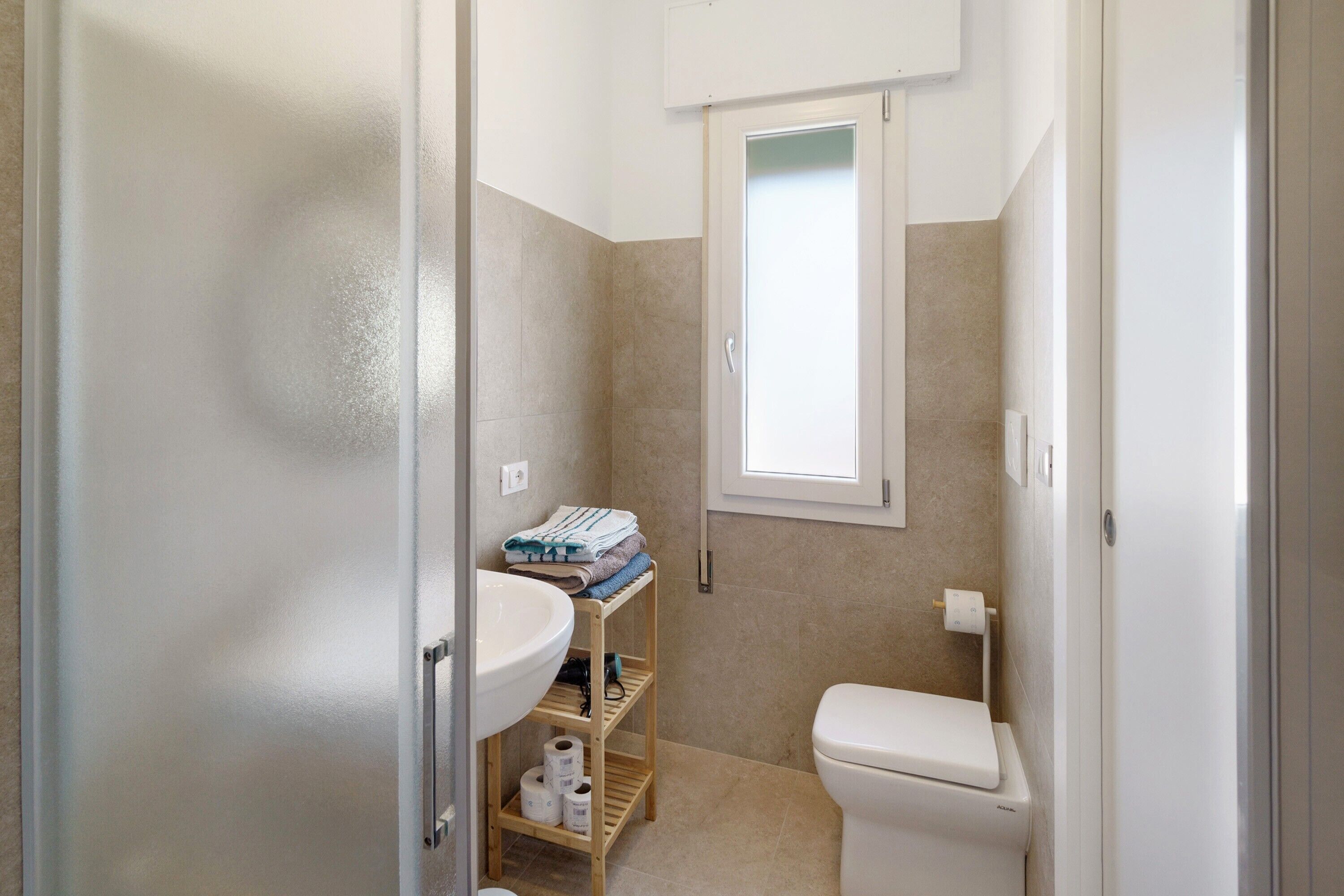 Ein Badezimmer mit Toilette, Waschbecken und Regalen mit Handtüchern und Toilettenpapier.