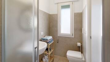 Ein Badezimmer mit Toilette, Waschbecken und Regalen mit Handtüchern und Toilettenpapier.