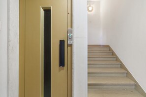 Una scala conduce a un ascensore, una porta con maniglia e un lampadario.