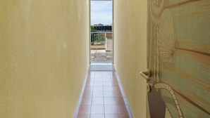 A narrow hallway with a tiled floor leading to a door with a view of a balcony and a railing. - Just Steps from the Beach – Cozy Apartment in Sottomarina (Chioggia)