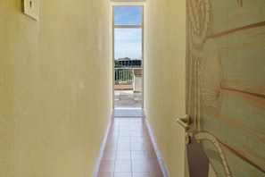Un corridoio stretto con pavimento piastrellato che conduce a una porta con vista su un balcone e una ringhiera.