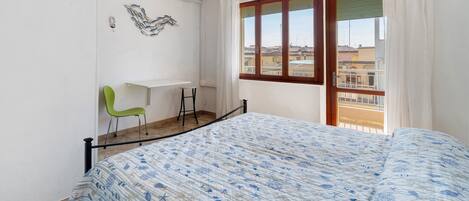 Un dormitorio con cama, escritorio, silla y ventana con vista.