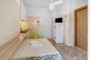 A kitchen with a white refrigerator, a wooden cabinet, a ceiling fan, and a door. - Just Steps from the Beach – Cozy Apartment in Sottomarina (Chioggia)