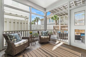 A covered porch with wicker furniture, a white picket fence, and a view of the neighborhood.