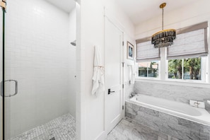 A modern bathroom with a shower, bathtub, and large window.