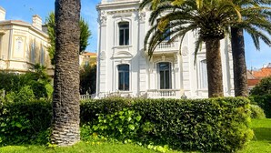 Un bâtiment blanc à la façade symétrique, entouré de pelouses bien entretenues et de palmiers.