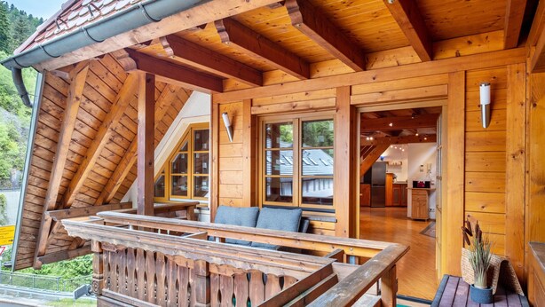 Une cabane en bois dotée d’un balcon, d’un coin repas et d’une cuisine visible à travers les fenêtres.