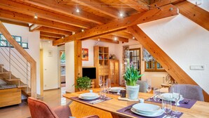Un coin repas avec une table en bois dressée pour quatre personnes, entourée de chaises, et un escalier menant à un autre niveau.