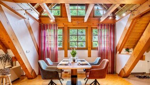Un coin repas avec une table en bois, quatre chaises et une vue sur les arbres à travers de grandes fenêtres.