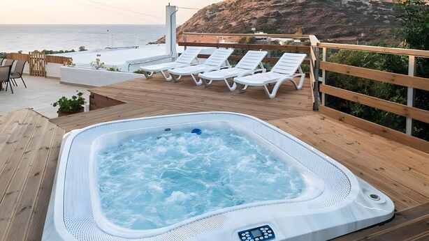 Un jacuzzi en una terraza de madera con sillones reclinables y vista al mar.