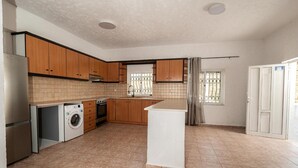 Una cocina con armarios de madera, lavadora, estufa y una ventana con cortinas.
