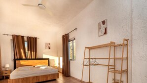 Un dormitorio con cama, una estantería de madera, una ventana con cortinas y una obra de arte en la pared.