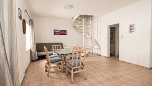Un comedor con una mesa de vidrio y sillas de madera, un sofá, una escalera en espiral y una puerta de baño.