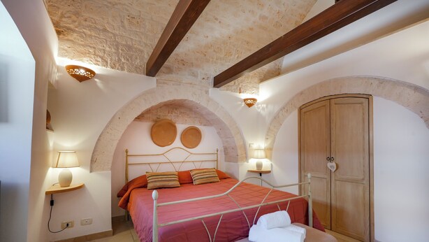 Ein Schlafzimmer mit Bett, einer Bank, einem Kleiderschrank und einer Steinsäule.
