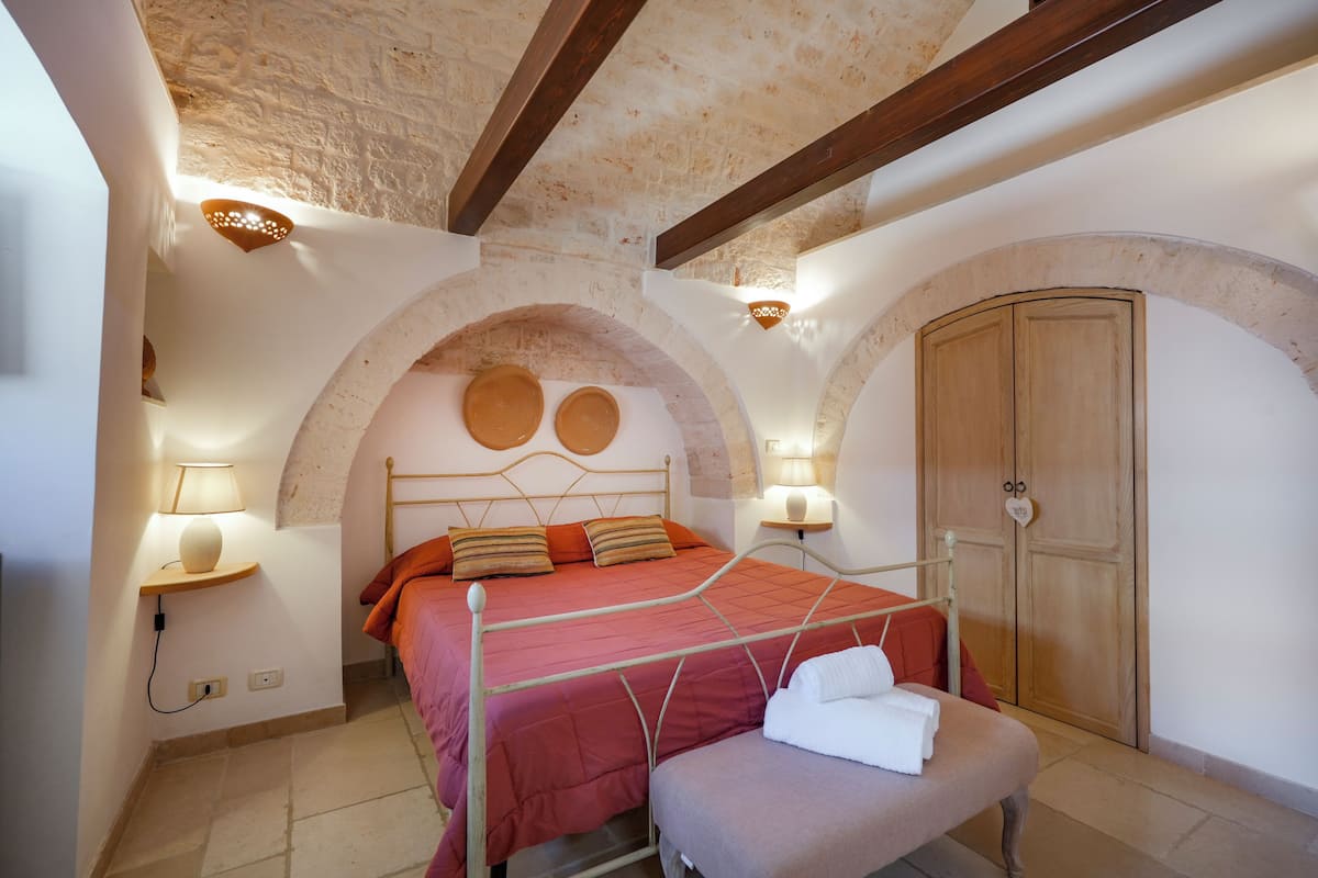 Una camera da letto con un letto, una panca, un armadio e un muro in pietra.