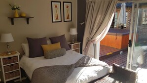 Ein Schlafzimmer mit Bett, Kissen, Nachttischen, einer Lampe, einer Vase mit Blumen, gerahmten Bildern und Blick auf eine Terrassenanlage.