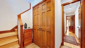 Un escalier en bois mène à une pièce dotée d’une grande porte en bois, d’une petite table sur laquelle se trouve une lanterne, et d’un couloir recouvert d’une moquette.