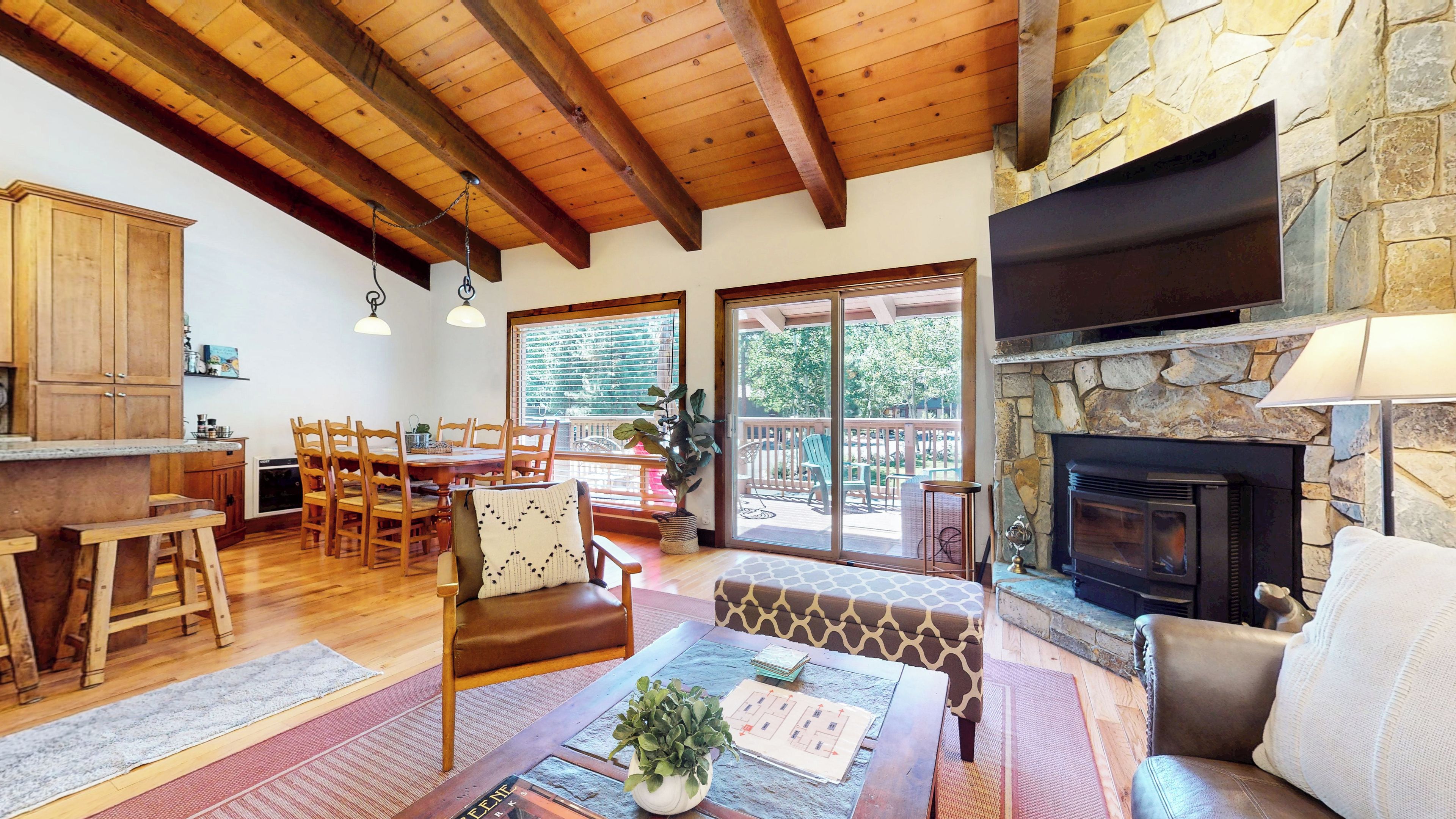 A spacious living area with a stone fireplace, wooden furniture, and a dining area with a view of the outdoors.