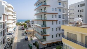 Un immeuble résidentiel à plusieurs étages, doté de balcons, d’un espace de stationnement et offrant une vue sur la mer.