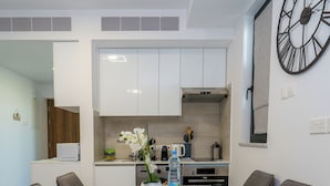 Une cuisine moderne avec des meubles blancs, une grande horloge et une table à manger avec quatre chaises.