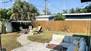 A backyard with a white sofa, two chairs, a small table, and a wooden fence. - Renovated Mid-Century Modern 3 bedroom Home with Fenced In Backyard in Orlando (Orlando)