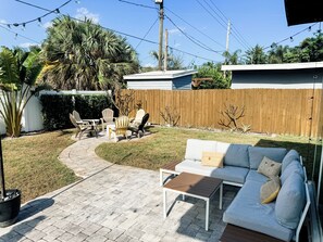 Ein Garten mit einer weißen Couch, zwei Stühlen, einem kleinen Tisch und einem Holzzaun.