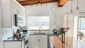 A kitchen with white cabinets, a wooden ceiling, a large window, and a wooden island. - Renovated Mid-Century Modern 3 bedroom Home with Fenced In Backyard in Orlando (Orlando)