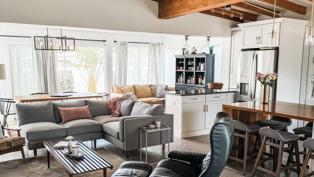 A spacious living area with a high ceiling, a sofa set, a coffee table, a leather chair, and a kitchen area with cabinets and a refrigerator. - Renovated Mid-Century Modern 3 bedroom Home with Fenced In Backyard in Orlando (Orlando)