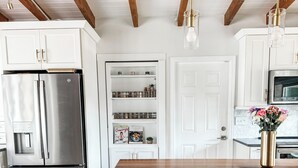 A modern kitchen with a wooden table, two bar stools, a stainless steel refrigerator, and a built-in pantry. - Renovated Mid-Century Modern 3 bedroom Home with Fenced In Backyard in Orlando (Orlando)