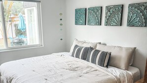 A bedroom with a bed, a wooden nightstand, a window with a view, and wall art. - Renovated Mid-Century Modern 3 bedroom Home with Fenced In Backyard in Orlando (Orlando)