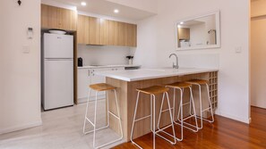 Eine moderne Küche mit einem weißen Kühlschrank, Holzschränken, einer weißen Arbeitsplatte und drei Barhocker.