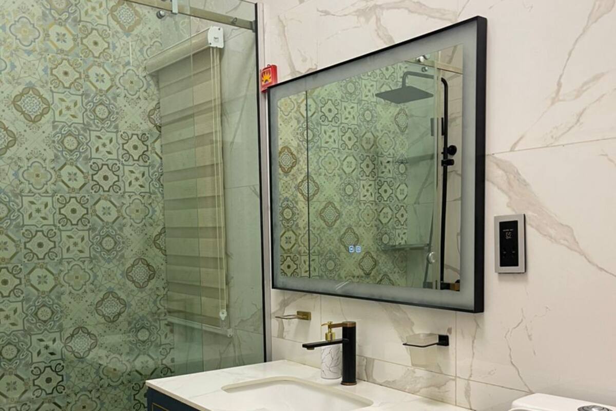 Un bagno con cabina doccia in vetro, un WC bianco, un mobile lavabo scuro con maniglie dorate e uno specchio sopra il lavello.