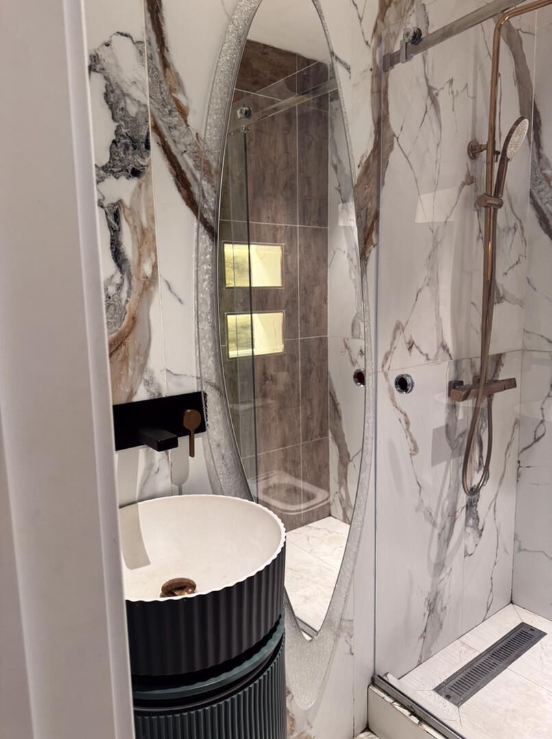 Un baño moderno con ducha de vidrio, paredes de mármol y tocador negro.