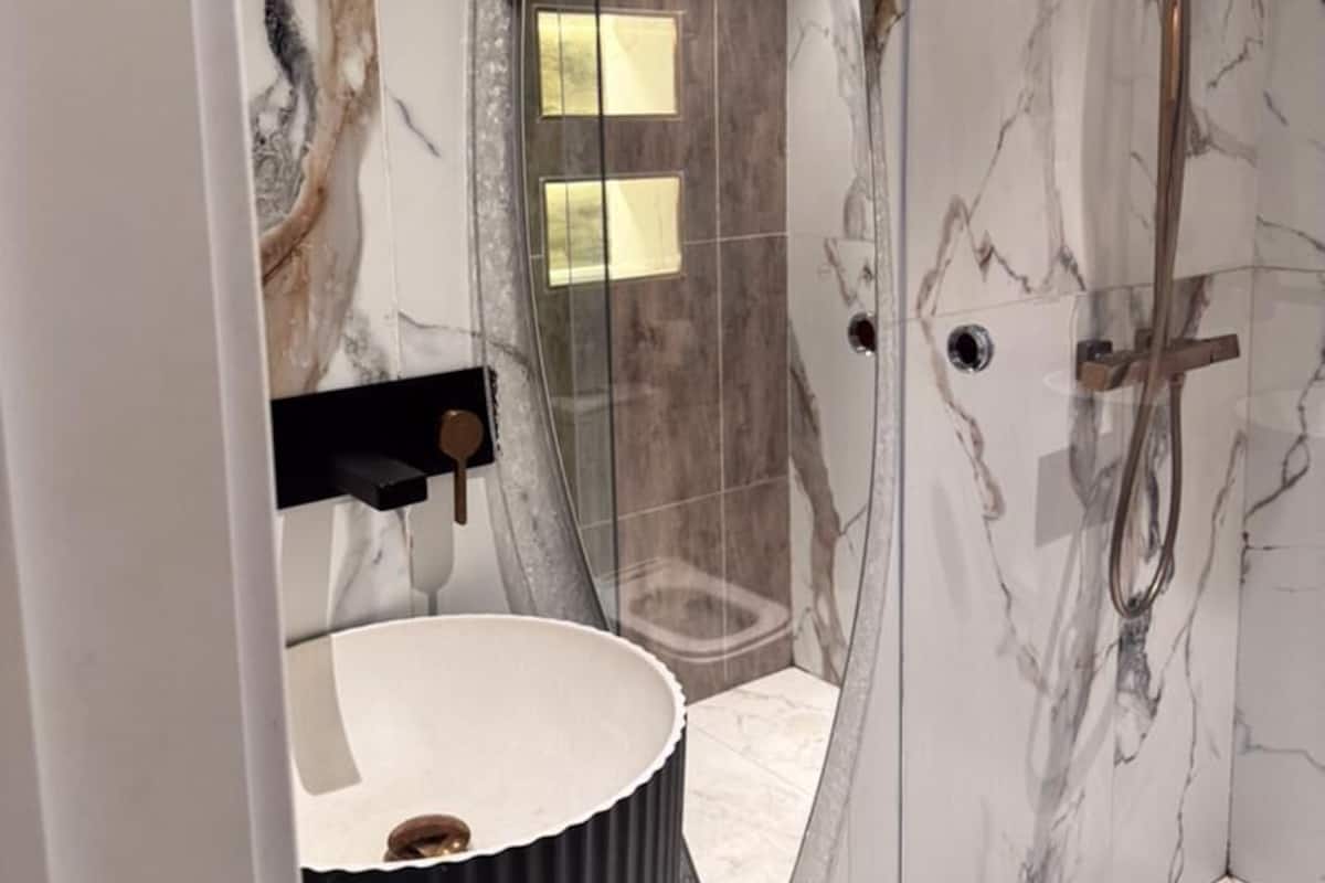 Un bagno moderno con cabina doccia in vetro, pareti in marmo e mobile lavabo nero.
