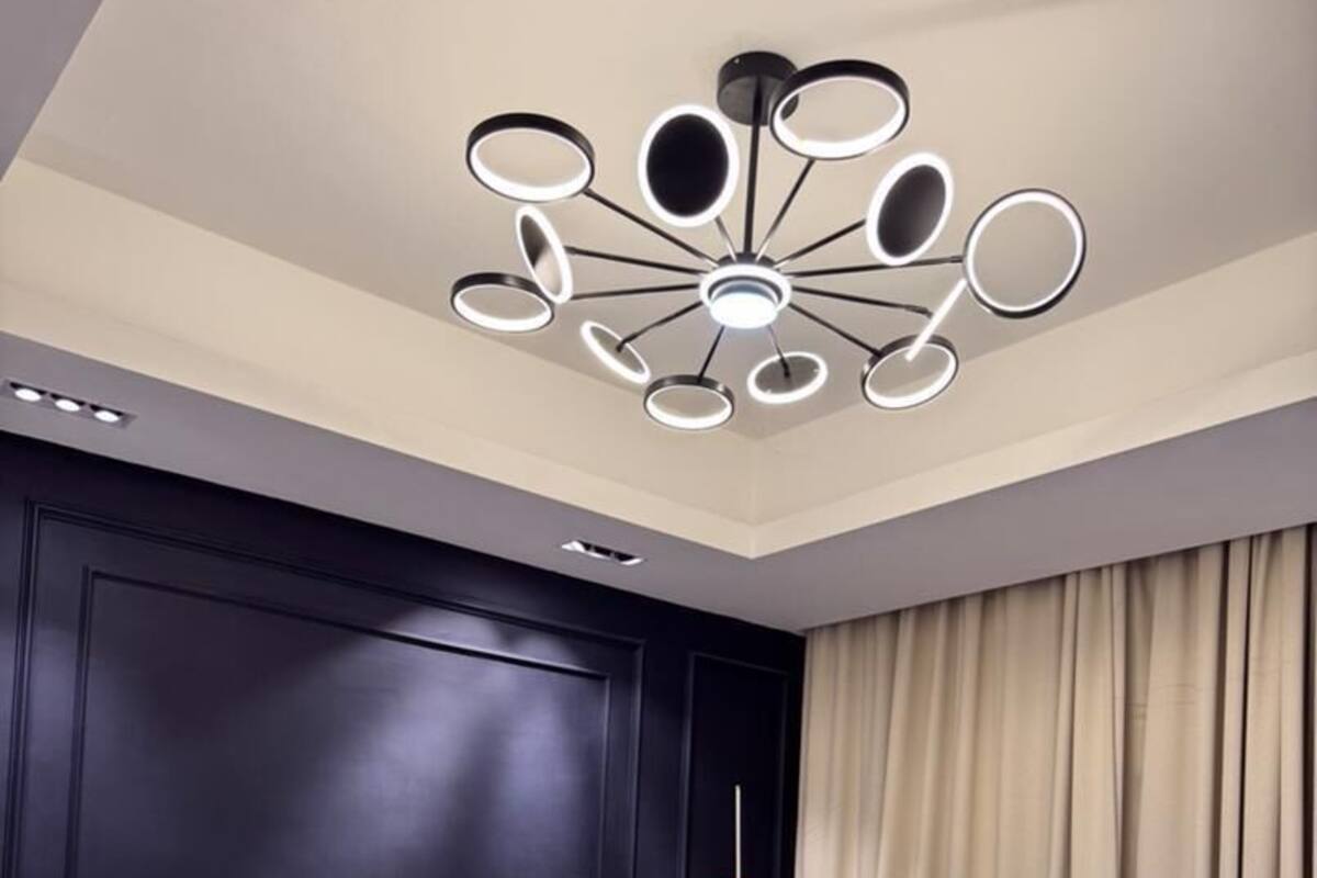 Una camera d'albergo moderna con una parete rivestita in legno scuro, un letto grande con biancheria da letto bianca e blu, una lampada a soffitto circolare particolare e una finestra con tende beige.