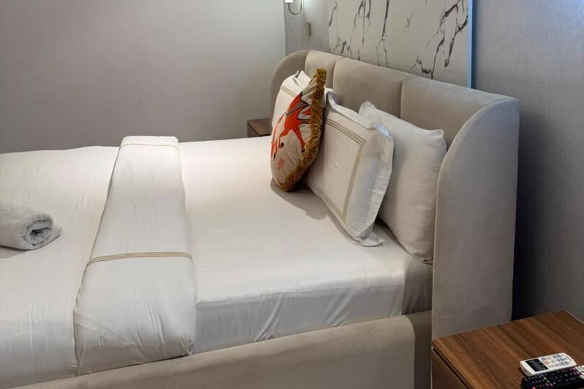 Una camera d'albergo moderna con un letto, un comodino, un telecomando e una parete con motivo marmorizzato.
