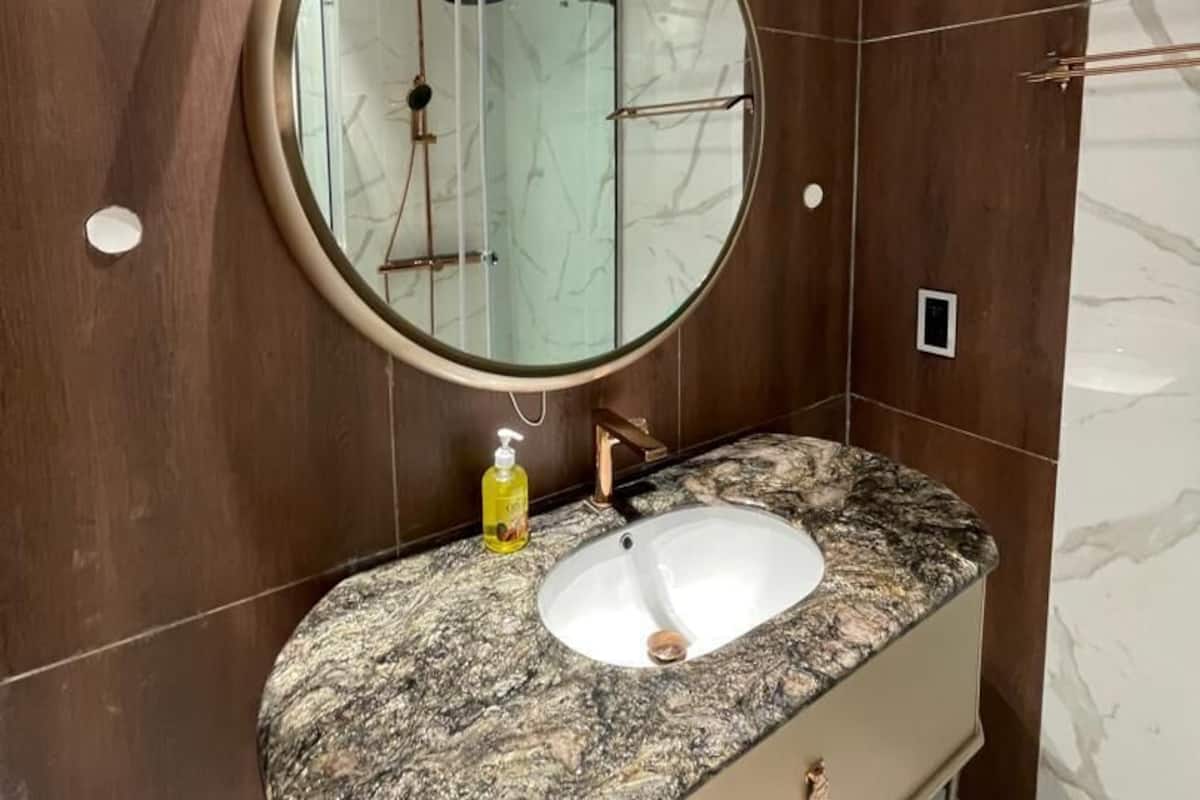 Un bagno con uno specchio rotondo, lavabo in marmo, mobile contenitore in legno e doccia.