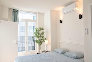 A bedroom with a bed, a window, a plant, and an air conditioning unit. - 12-guest Apartment on the Main Square (Antwerp)