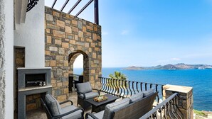 A stone-walled outdoor seating area with a fireplace, overlooking a body of water and a distant island. - Yalıkavakta 3 Odalı Villa BD4148 (Bodrum)