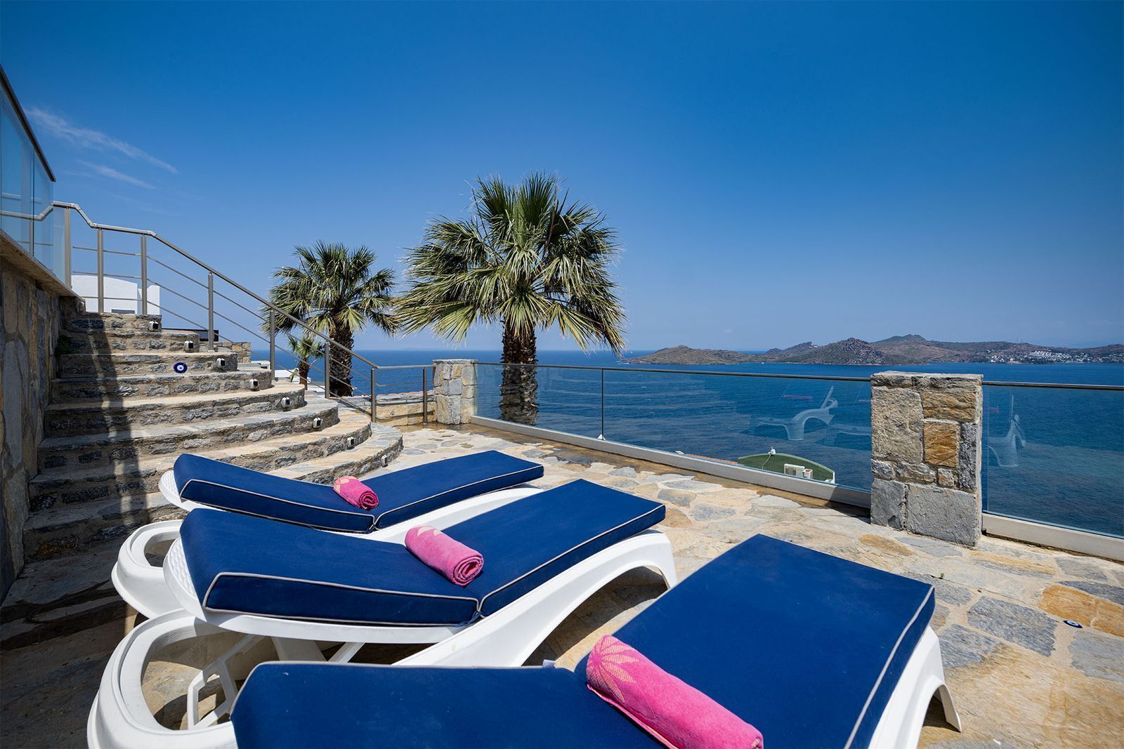 A terrace with sun loungers, a stone staircase, and a view of the sea.