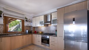 A modern kitchen with wooden cabinets, a stainless steel refrigerator, a microwave, and a gas stove. - Yalıkavakta 3 Odalı Villa BD4148 (Bodrum)