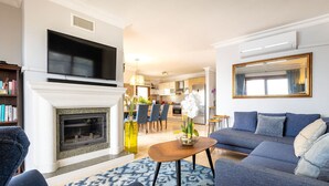 A living room with a fireplace, a TV mounted on the wall, a sofa, and a dining area with chairs. - Yalıkavakta 3 Odalı Villa BD4148 (Bodrum)
