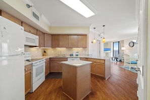 A modern kitchen with wooden cabinets, a built-in island, and a view to the living area. - White Caps 1006 by Liquid Life (Orange Beach)